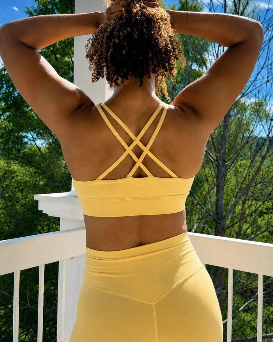 Person wearing a yellow sports bra and shorts on a balcony with trees in the background