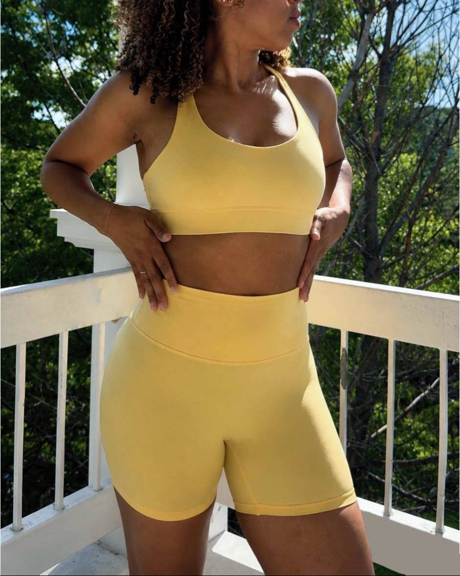 Woman in yellow athletic wear standing on a balcony with trees and blue sky in the background