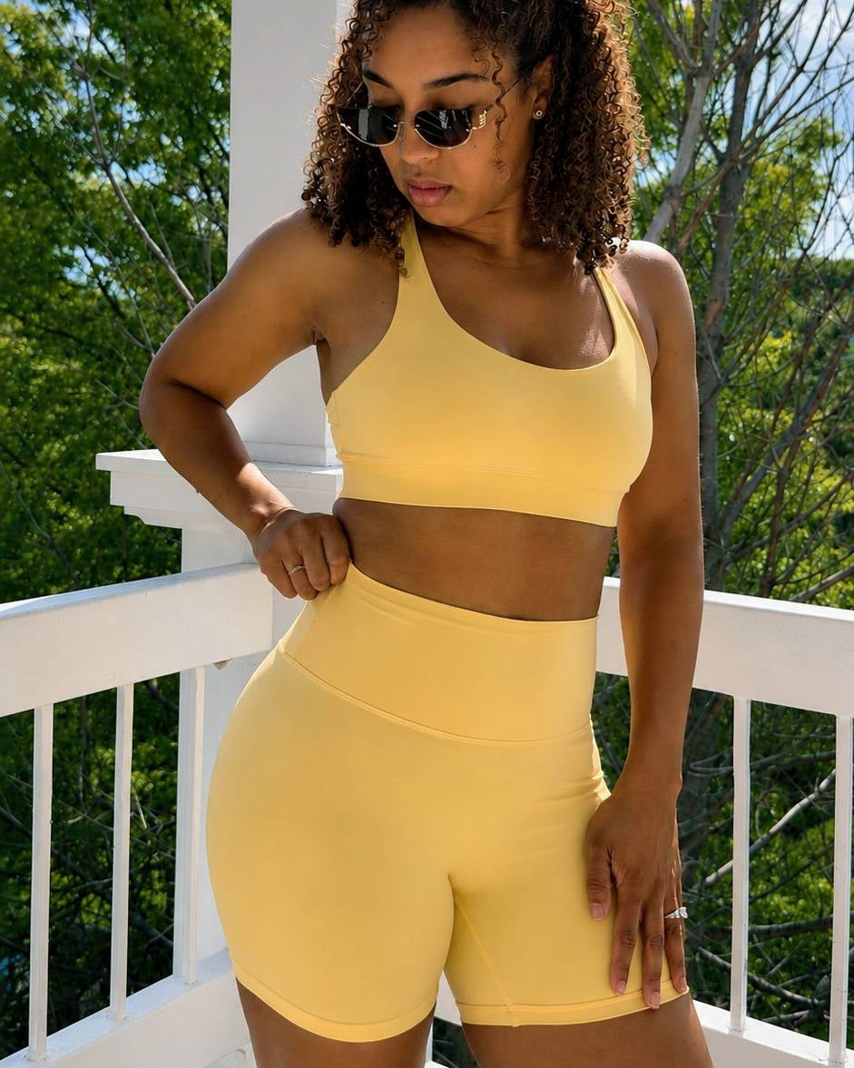 Woman wearing a yellow sports bra and shorts set on a balcony with trees in the background