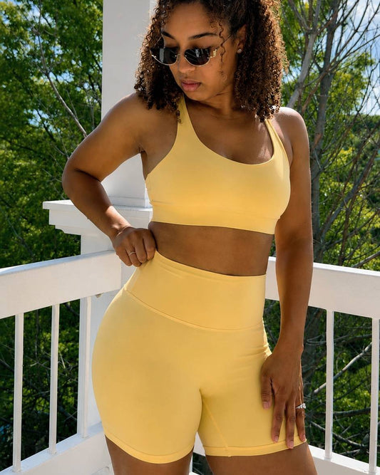 Woman wearing a yellow sports bra and shorts set on a balcony with trees in the background
