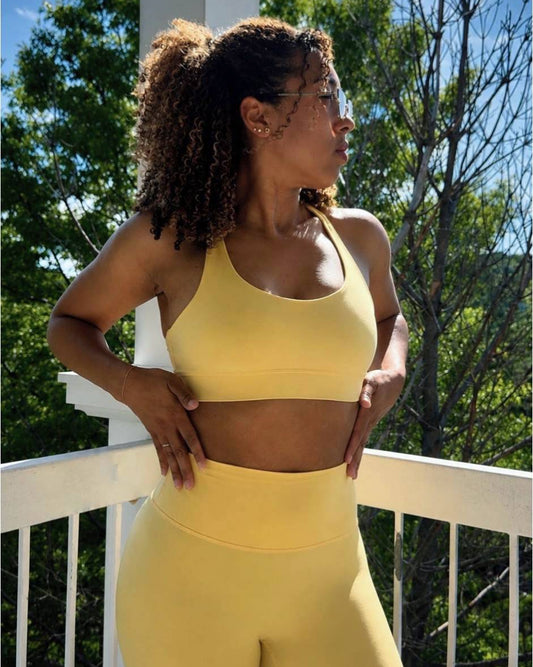 Woman in yellow athletic wear standing on a balcony with trees and blue sky in the background