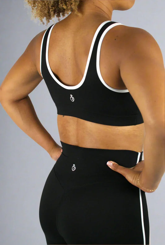 Person wearing a black sports bra and leggings with a white logo on a light gray background