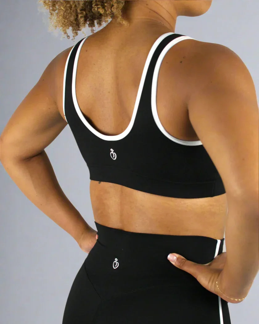 Person wearing a black sports bra and leggings with a white logo on a light gray background
