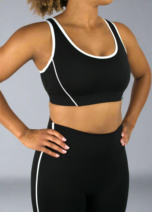 Person wearing a black sports bra and leggings with white accents on a plain background