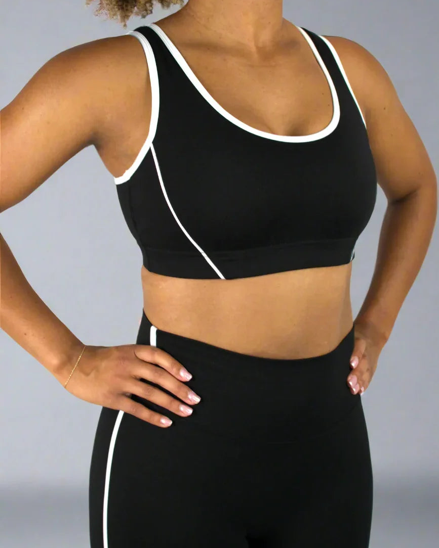 Person wearing a black sports bra and leggings with white accents on a plain background