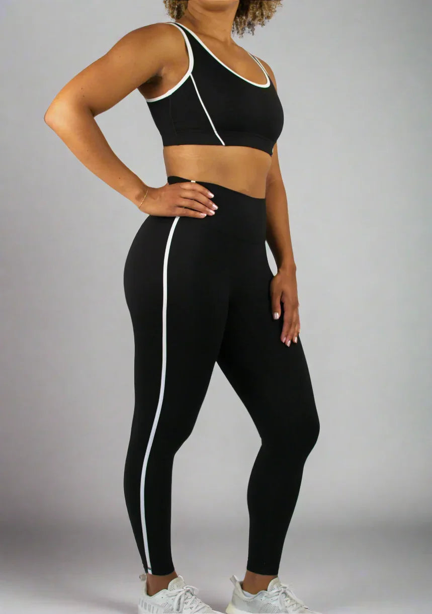 Person wearing a black sports bra and leggings with white accents on a plain background