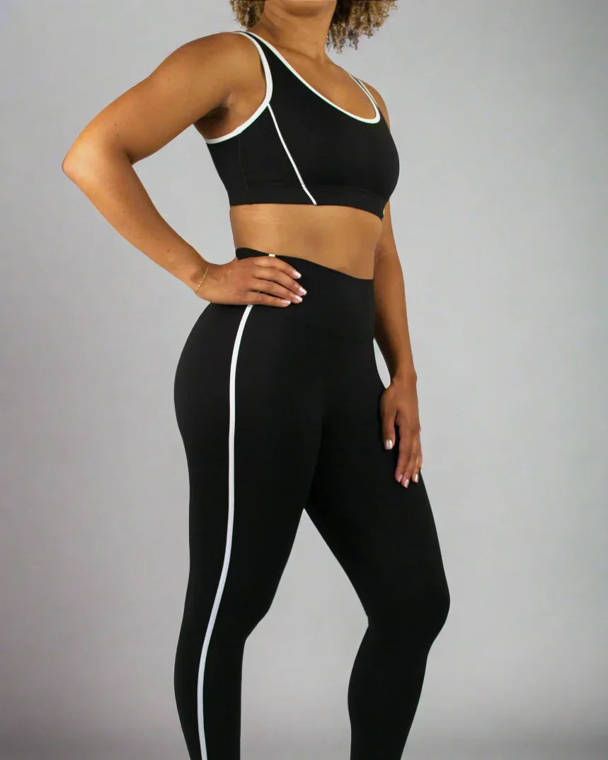 Person wearing a black sports bra and leggings with white accents on a plain background