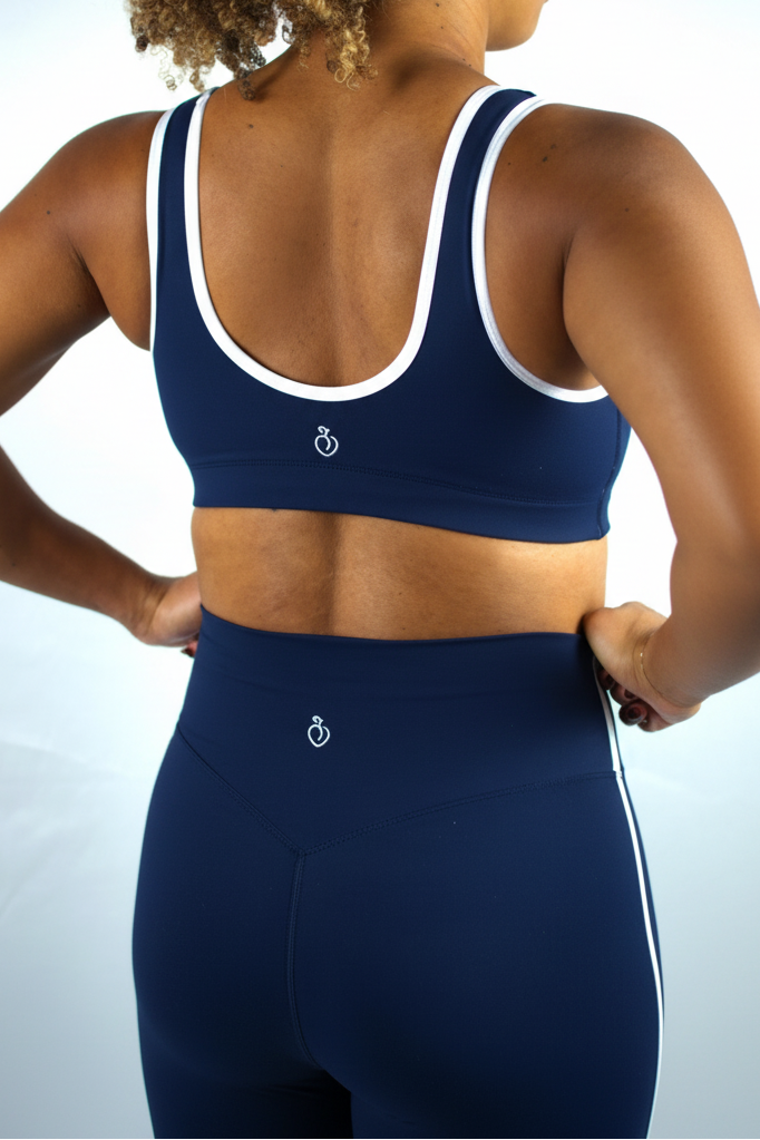Person wearing a navy blue sports bra and leggings with a white logo on a light gray background