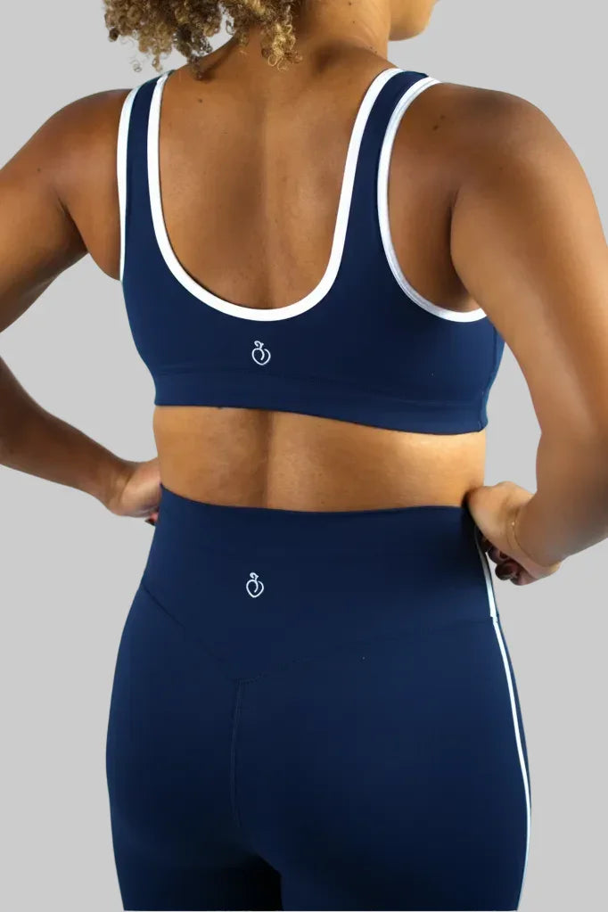 Person wearing a navy blue sports bra and leggings with a white logo on a light gray background