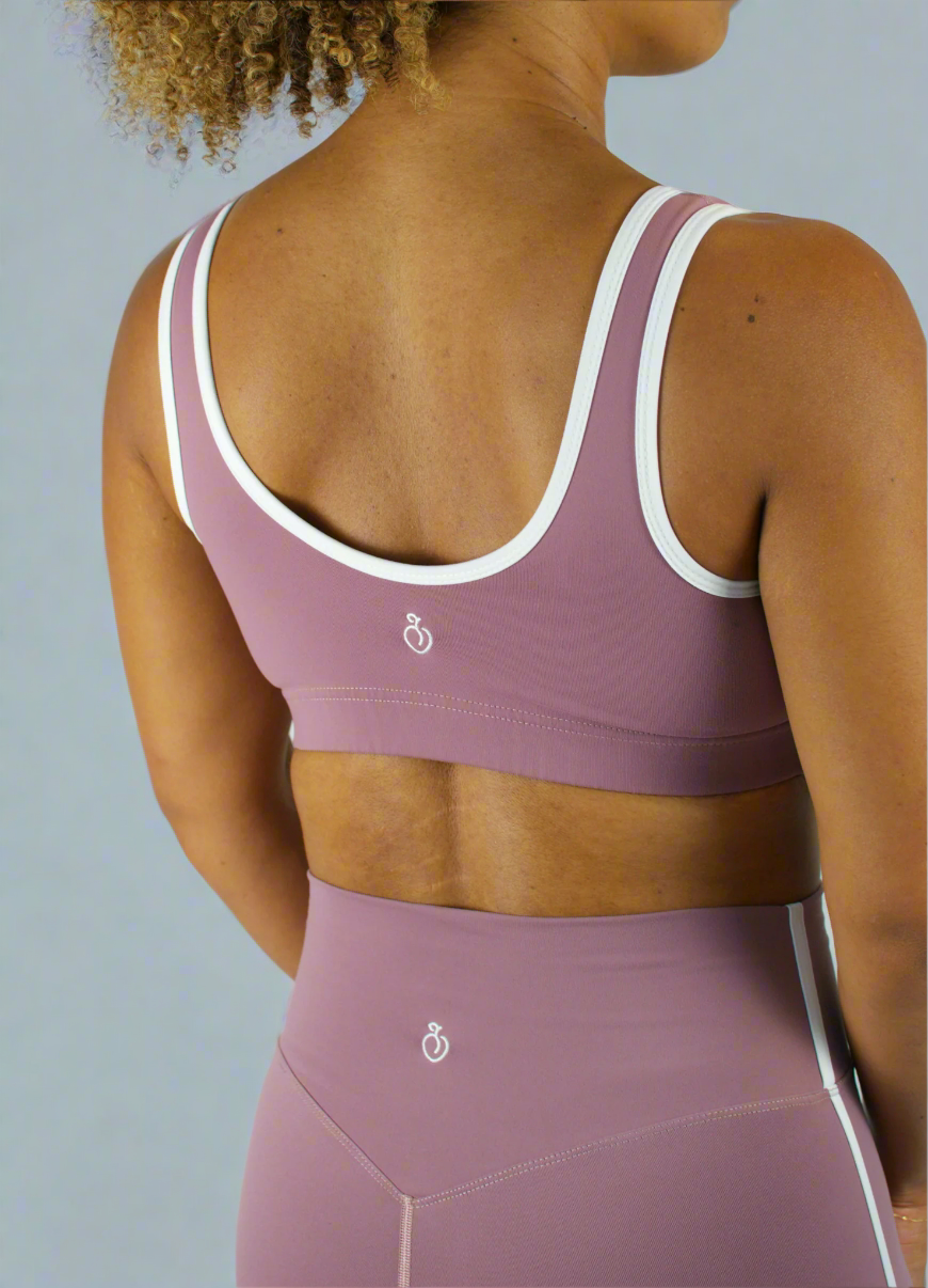 Person wearing a mauve sports bra and leggings with white accents on a light gray background