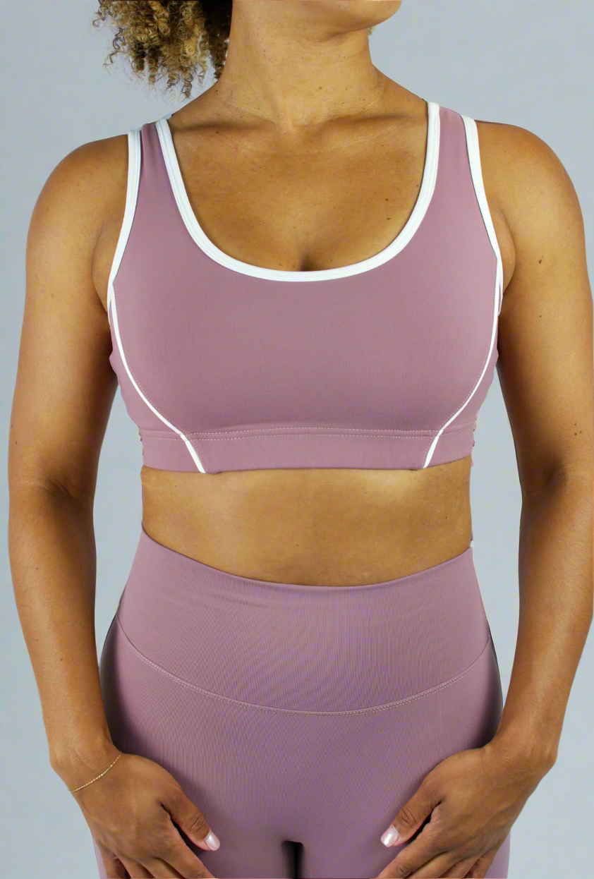Person wearing a mauve sports bra and leggings set on a plain background
