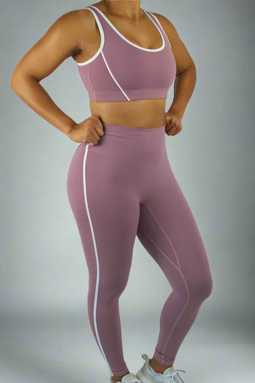 Person wearing a mauve sports bra and leggings with white accents on a plain background