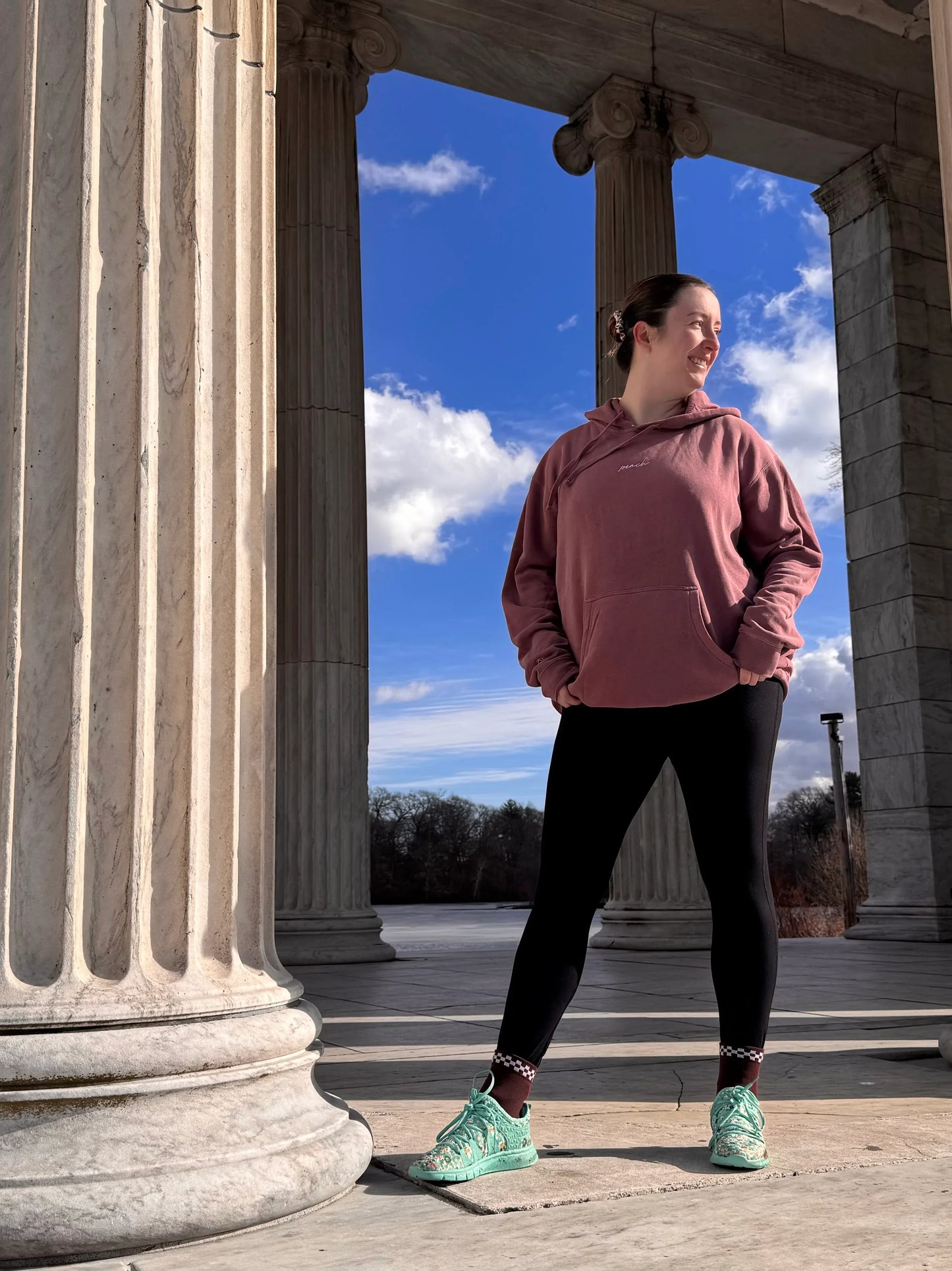 Woman in Peach Active hoodie and black leggings standing by marble columns outdoors