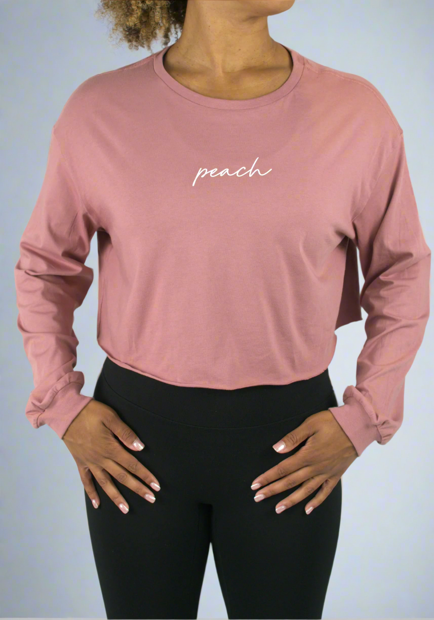 Person wearing a pink long-sleeve crop top with 'peach' text on a light gray background
