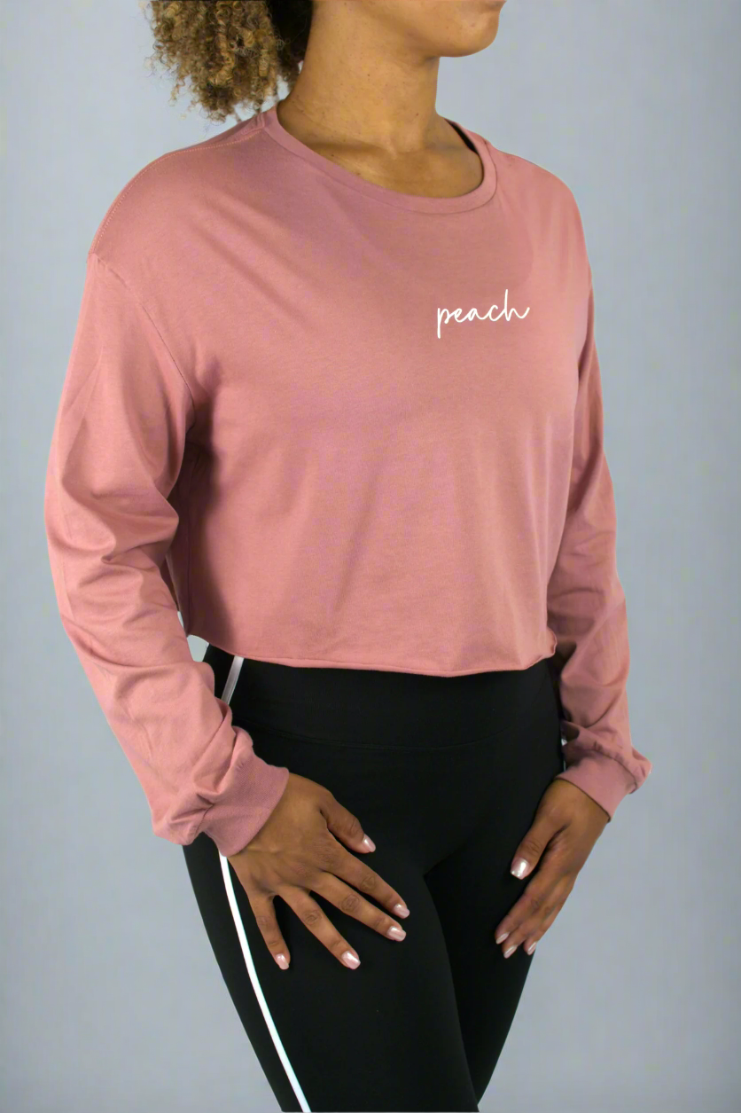Person wearing a pink long-sleeve crop top with 'peach' text on a white background