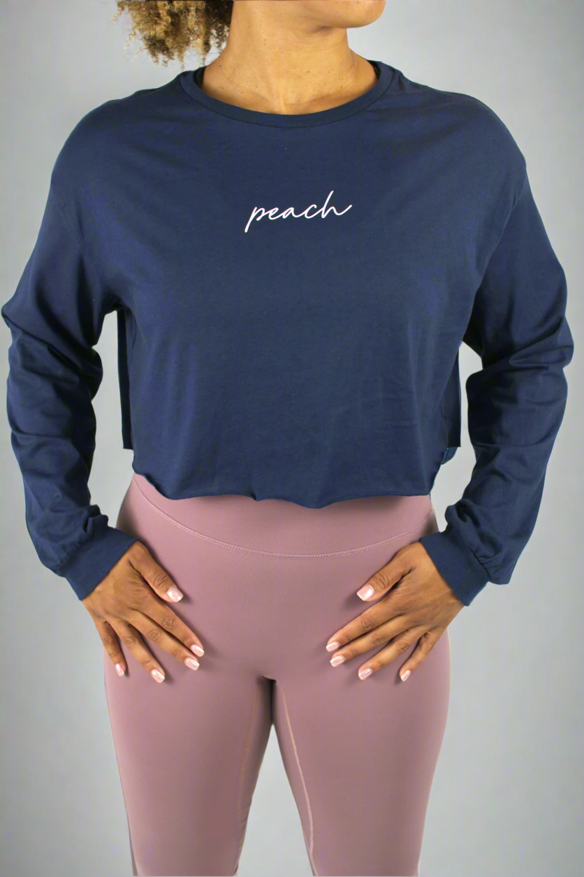 Person wearing a navy long-sleeve crop top with 'peach' text and pink leggings on a white background