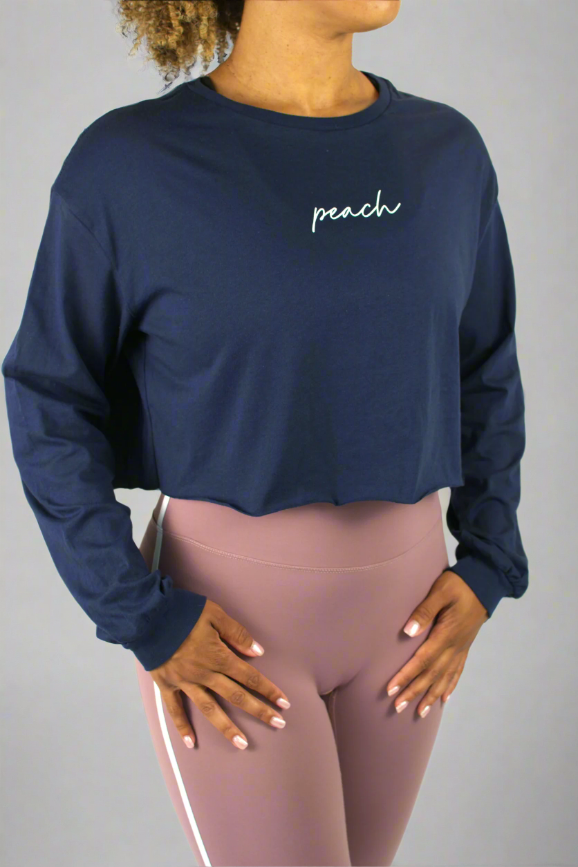 Person wearing a navy long-sleeve crop top with 'peach' text and pink leggings on a white background