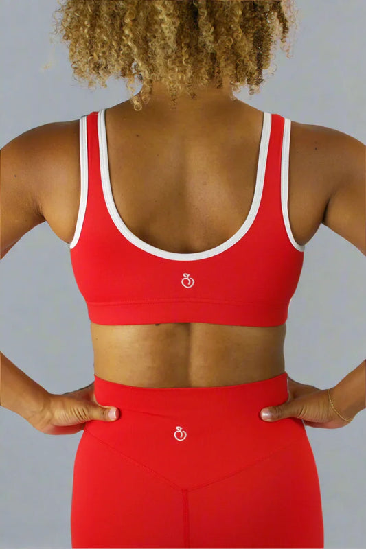 Person wearing a red sports bra and leggings with a white logo on a plain background