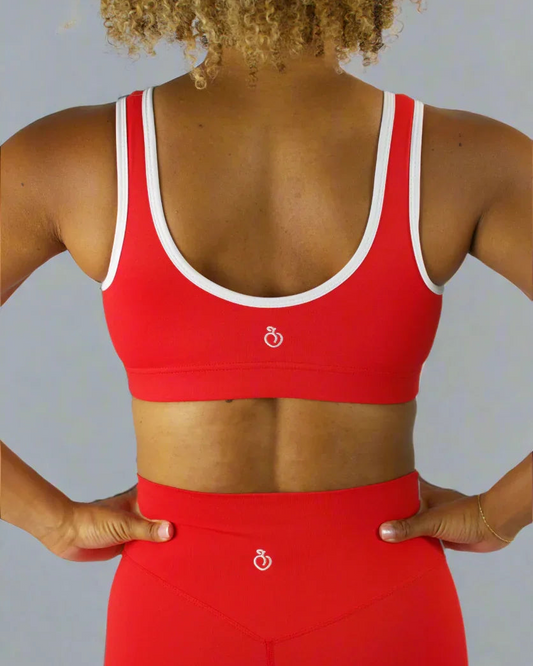Person wearing a red sports bra and leggings with a white logo on a plain background