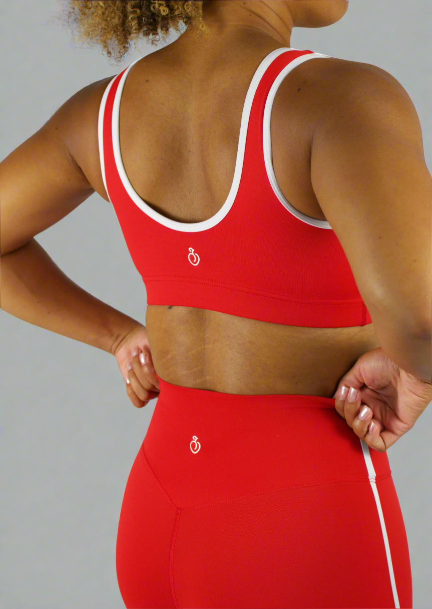 Person wearing a red sports bra and leggings set with a logo on a plain background
