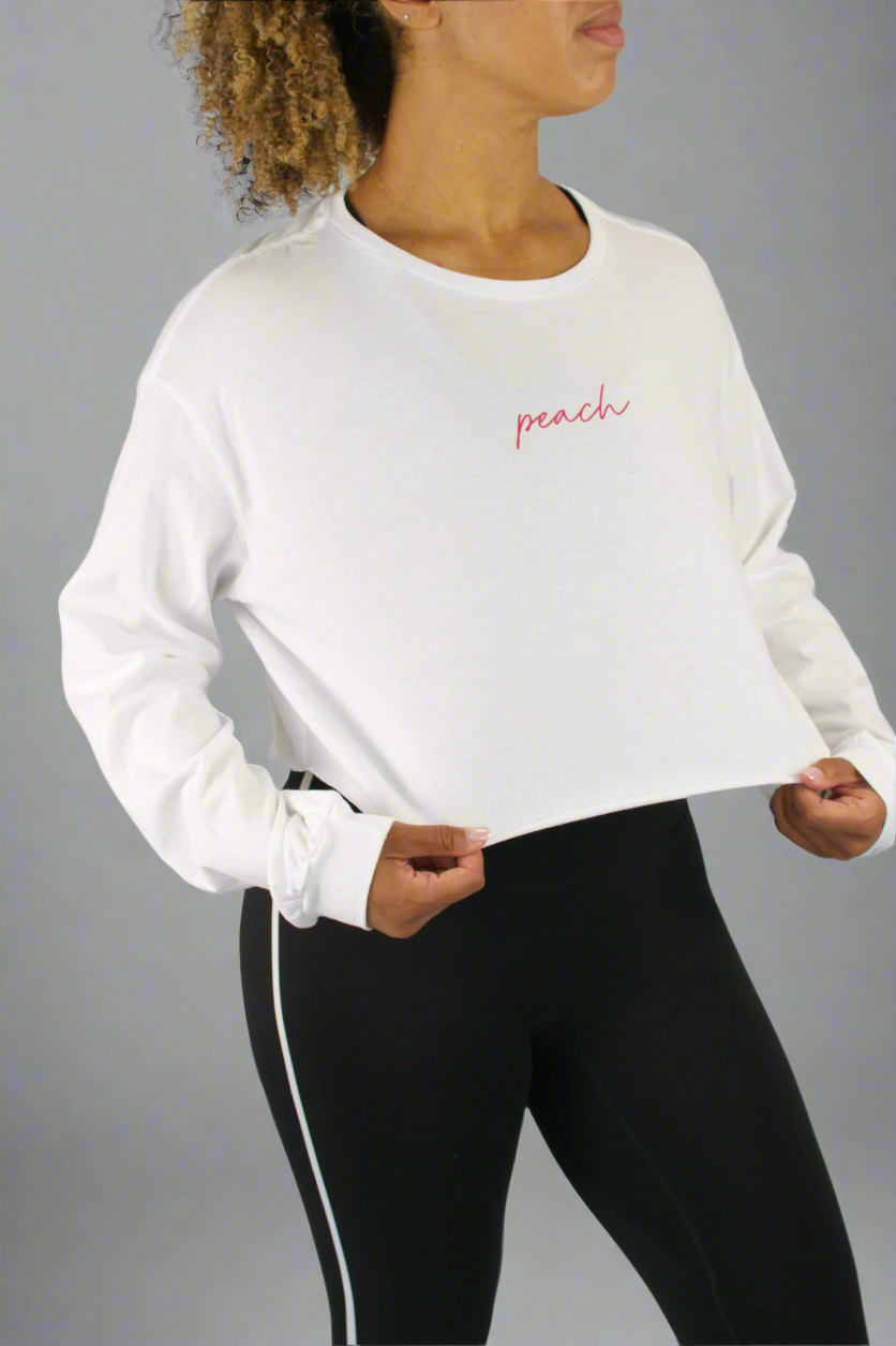 Person wearing a white long-sleeve shirt with 'peach' text and black leggings on a gray background