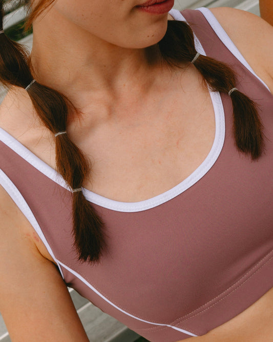 Close-up of a woman wearing a dusty mauve sports bra with white trim, featuring her braided hair and neck.