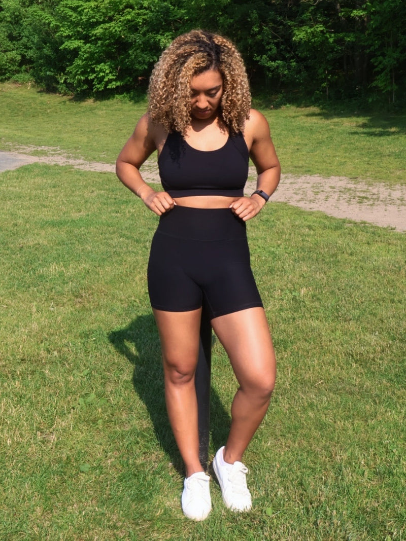 Person wearing a black athletic outfit standing on grass with trees in the background