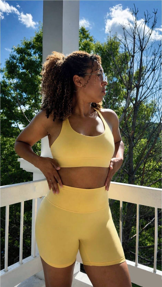 Woman in yellow athletic wear standing on a balcony with trees and blue sky in the background