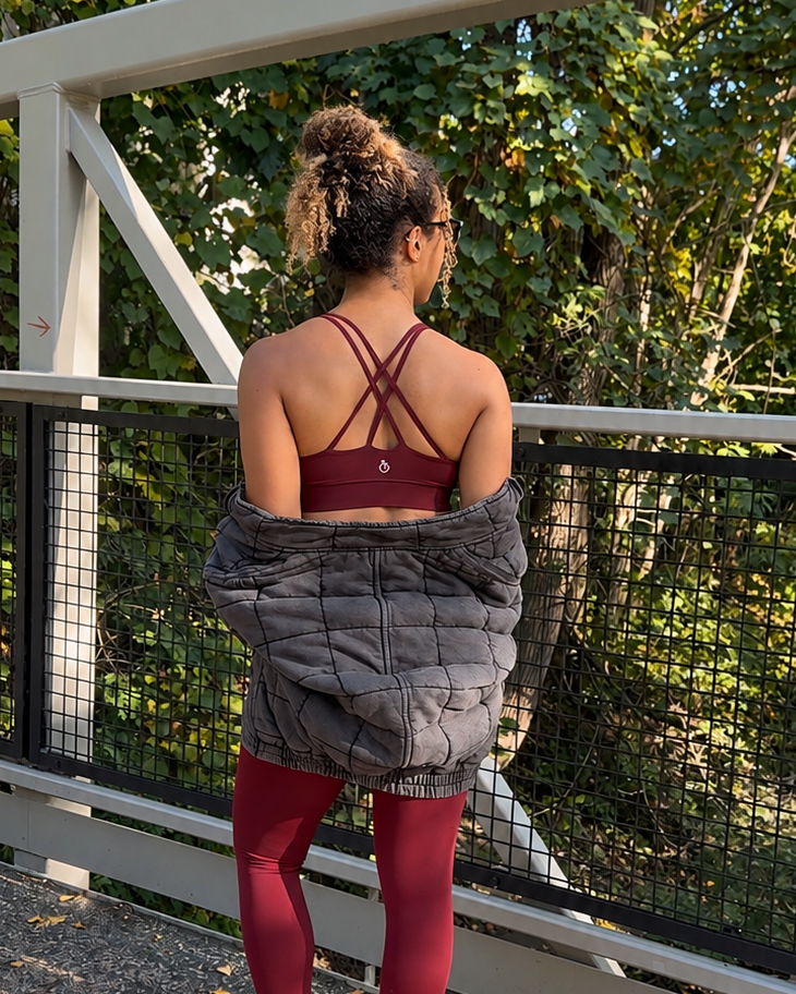 Woman in maroon sports bra, leggings, and black jacket showing detail of crossback sports bra
