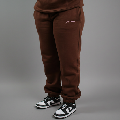 Brown sweatpants with 'peach' embroidery on a white background
