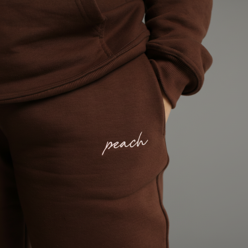 Brown tracksuit with 'peach' embroidery on a white background