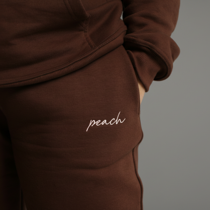 Brown tracksuit with 'peach' embroidery on a white background