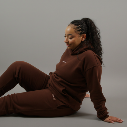 Person wearing a brown hoodie and pants sitting on a white background