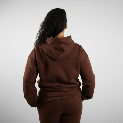 Person wearing a brown hoodie and pants against a white background