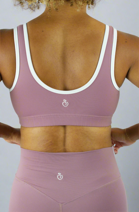 Person wearing a pink sports bra and leggings with a white logo on a light gray background