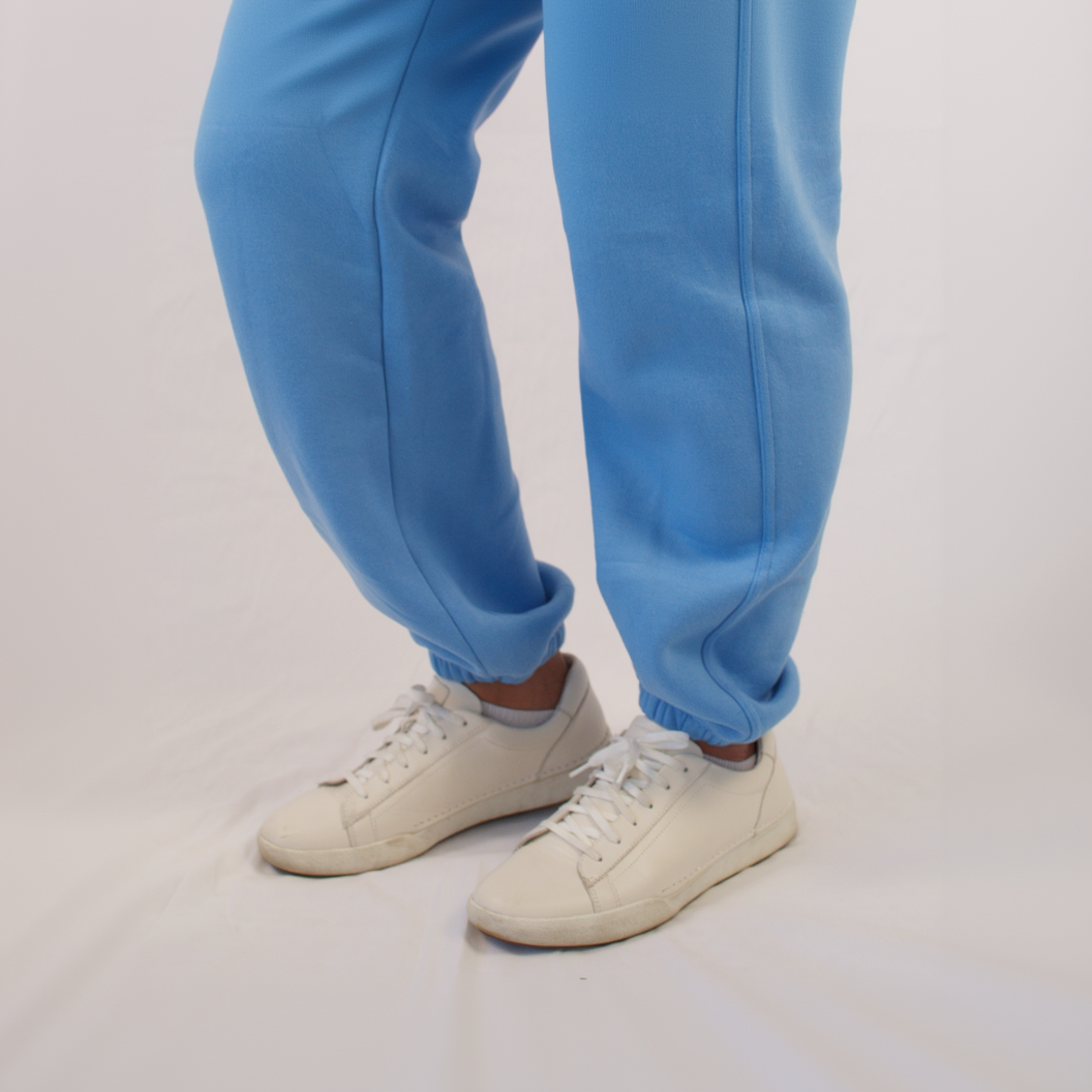 Blue sweatpants worn with white sneakers on a light gray background