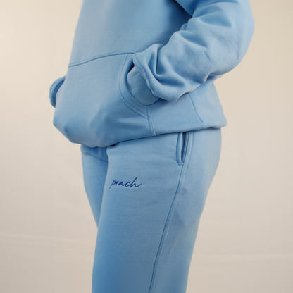 Light blue tracksuit with 'peach' embroidery on beige background