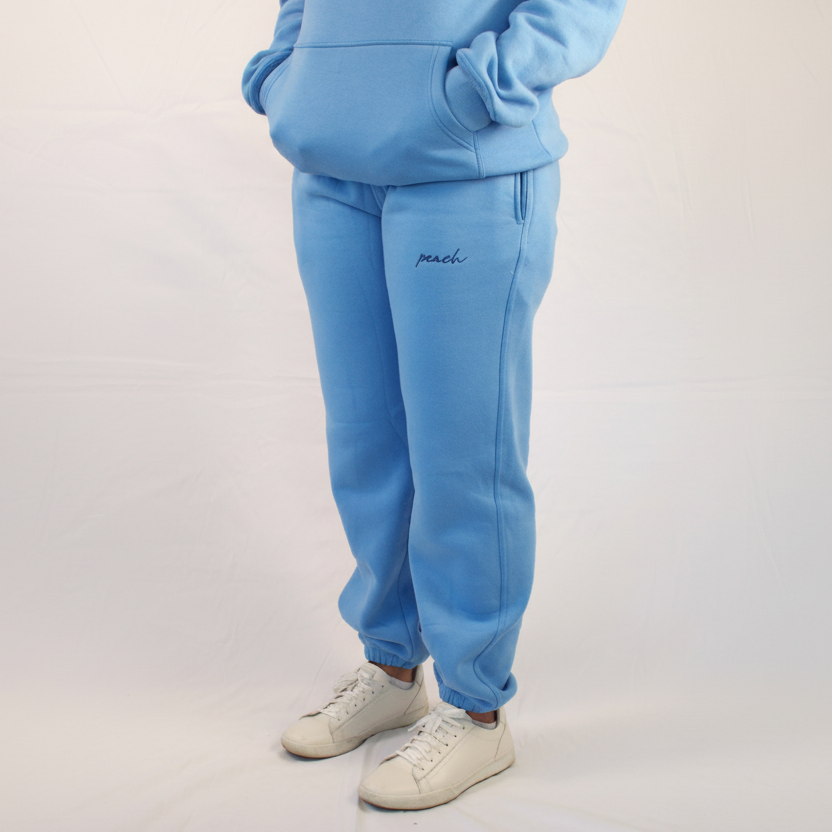 Light blue tracksuit with 'peach' embroidery on pants against a plain background