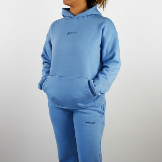 Person wearing a blue tracksuit with 'peach' branding on a plain background