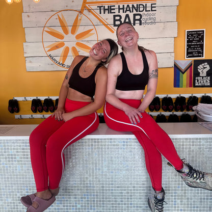 Two people posing in front of a 'The Handle Bar' sign on a yellow wall.
