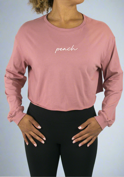 Person wearing a pink long-sleeve crop top with 'peach' text on a light gray background