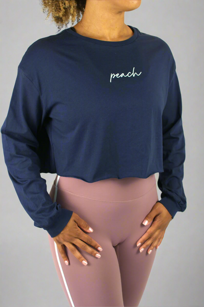 Person wearing a navy long-sleeve crop top with 'peach' text and pink leggings on a white background
