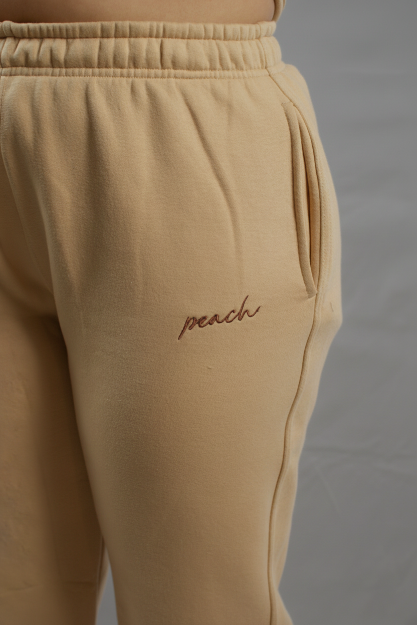 Beige sweatpants with 'peach' embroidery on a white background