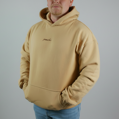 Person wearing a beige hoodie with 'peach' embroidery on a plain background