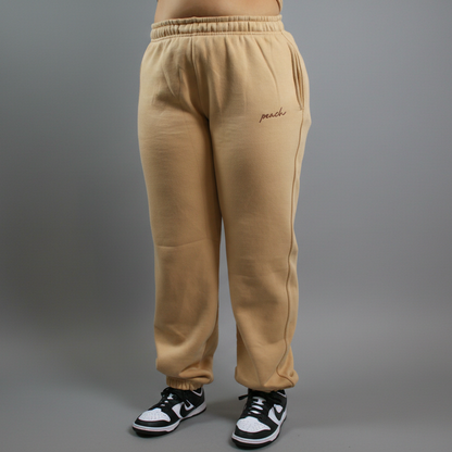 Beige sweatpants with 'peach' embroidery on a white background