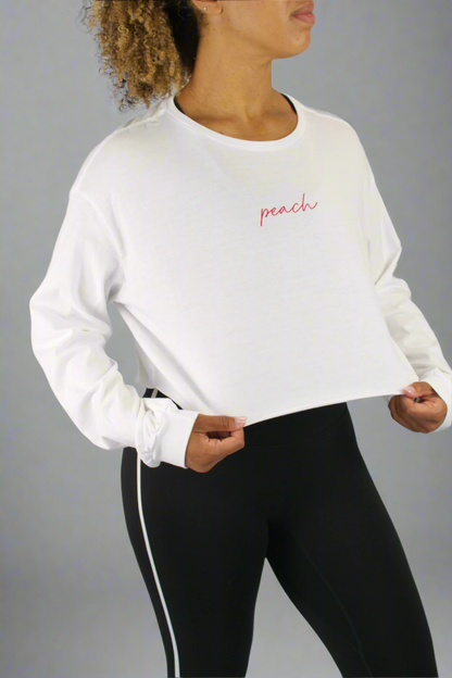 Person wearing a white long-sleeve shirt with 'peach' text and black leggings on a gray background